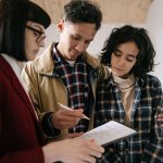 Casal analisa documentos de um imóvel com um profissional do mercado imobiliário dentro de um apartamento.
