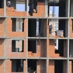 Trabalhadores constroem paredes de tijolos em um edifício residencial ainda inacabado.