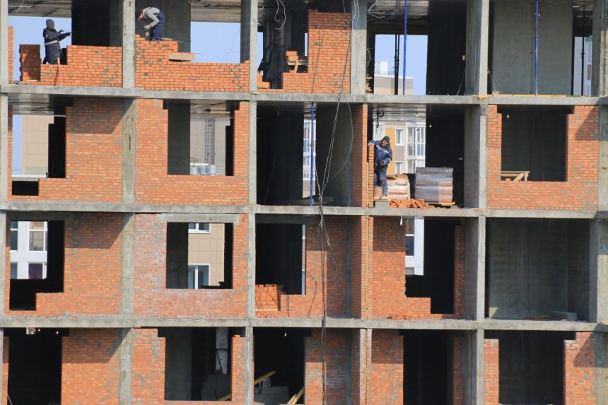 Trabalhadores constroem paredes de tijolos em um edifício residencial ainda inacabado.