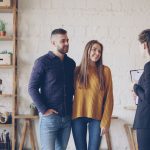 Casal conversa com uma corretora de imóveis em um ambiente interno durante uma consulta sobre opções de moradia.